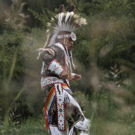 Native American dancer in a grassy field dressed in traditional wear